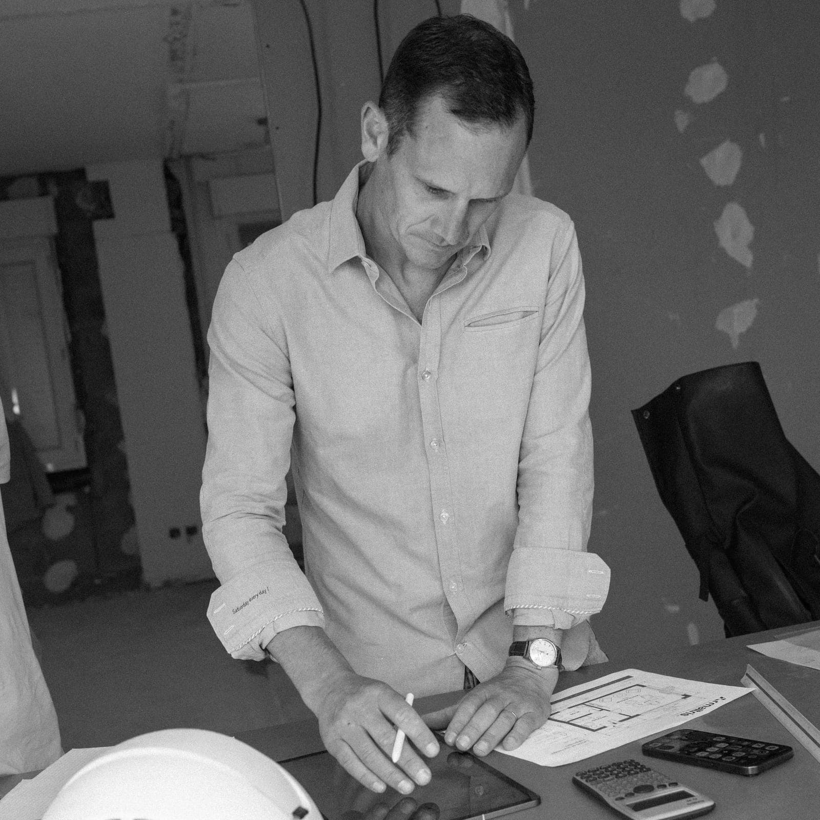 Jérôme Pollet annote un plan sur tablette, casque de chantier posé sur la table