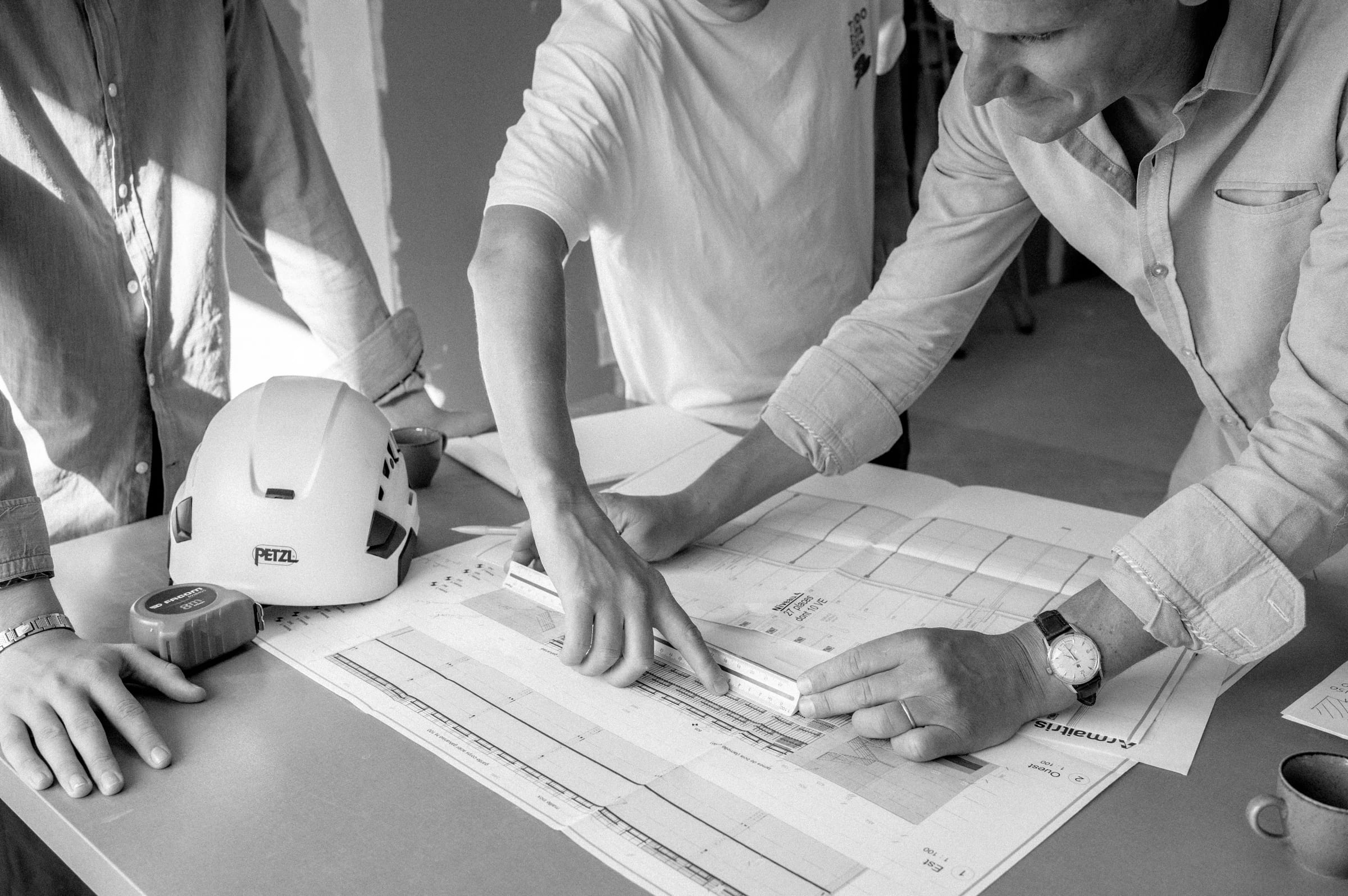 Lecture des plans à l’échelle autour de la table, casque de chantier posé à côté